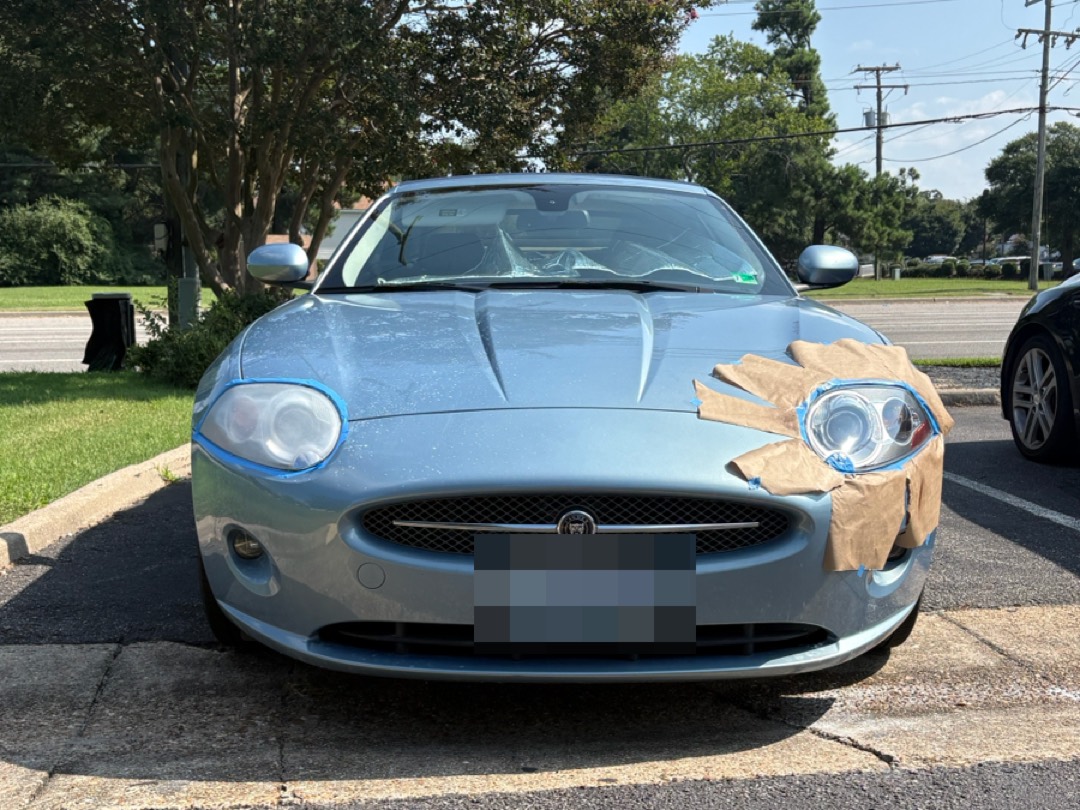 Jaguar XK with one headlight masked off with paper and tape, part way through a restoration.